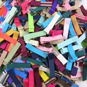 May include: A large assortment of colorful ribbon hair clips. The clips are made of various colors, including pink, blue, green, red, yellow, and purple. The clips are all about 2 inches long and have a metal clasp.