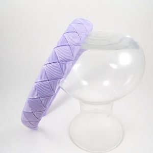 May include: A lavender headband with a woven design. The headband is made of a soft, pliable material and is perfect for adding a touch of color to any outfit.