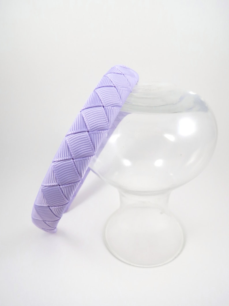May include: A lavender headband with a woven design. The headband is made of a soft, pliable material and is perfect for adding a touch of color to any outfit.