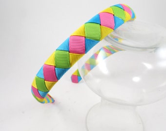 May include: A braided headband with yellow, green, pink, and blue ribbon. The headband is made of woven ribbon and is a bright and colorful accessory.