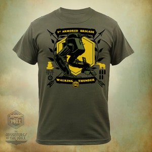 Op de afbeelding: Een groen T-shirt met een gele en zwarte afbeelding van een lopende tank. De afbeelding bevat de tekst "1st Armored Brigade", "VR-10 1933", "Walking Thunder" en "1911".
