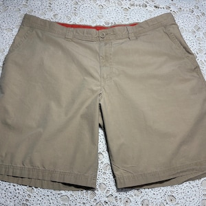 May include: Khaki-coloured shorts with a button closure and pockets. The shorts have a classic design and are made of a durable fabric. The waistband has a red lining. Suitable for casual wear.