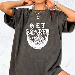 May include: Dark grey t-shirt featuring the text "GET SCARED" in a gothic font above a white jawbone graphic with a rose. The shirt has a vintage, washed appearance.
