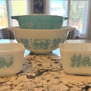 Puede incluir: Un conjunto de cuencos y platos cuadrados Pyrex vintage. Los cuencos son blancos y turquesas, con diseños decorativos de personas y gallos. El conjunto incluye dos platos cuadrados y tres cuencos de varios tamaños, perfectos para la cocina.