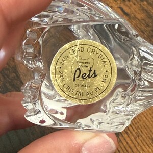 May include: A clear 24% lead crystal figurine with a circular gold sticker on the base. The sticker features the text Princess House Pets, 24% Lead Crystal, 24% Cristal Au Plomb, and Germany. The crystal has a faceted, textured surface design.