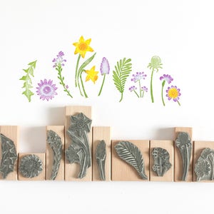 May include: A set of 10 wood mounted rubber stamps featuring floral designs. The stamps are arranged in a row on a white background. The designs include daffodils, ferns, and various wildflowers.