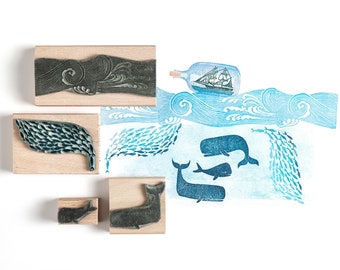 May include: A set of wooden stamps featuring a whale, a school of fish, a wave, and a bottle with a ship inside. The stamps are on a white background.