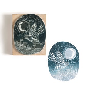 May include: A wooden block stamp with a detailed illustration of an owl flying under a crescent moon. The owl is in flight with its wings spread wide. The background is a dark blue with a church building and a field of grass.
