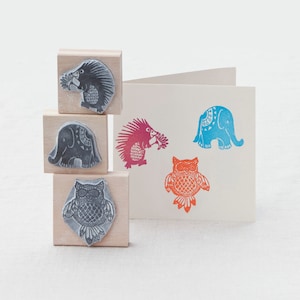 May include: Four wooden blocks with different animal designs. The blocks feature a gray hedgehog, a gray elephant, a red hedgehog, and a blue elephant. The blocks are stacked on top of each other.