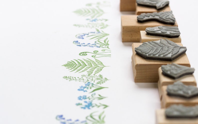 May include: A set of wooden mounted rubber stamps featuring various floral and fern designs. The stamps are arranged in a row on a white surface.