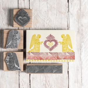Könnte beinhalten: Ein Satz mit vier Holz-Stempeln aus Gummi mit Engeln und einem Herzen mit dem Text "Live Peace Joy". Die Stempel befinden sich auf einem weißen Holzgrund.