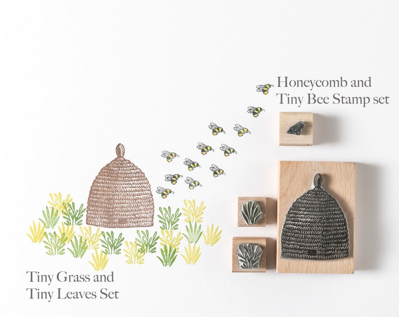 May include: A set of rubber stamps featuring a beehive, bees, grass, and leaves. The stamps are on wooden blocks. The text "Honeycomb and Tiny Bee Stamp set" and "Tiny Grass and Tiny Leaves Set" is printed below the stamps.