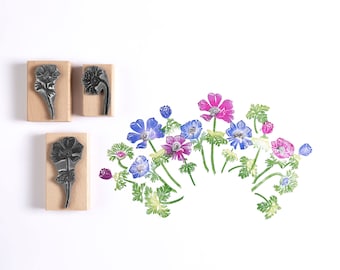 May include: Three wooden blocks with carved images of blue and pink flowers. The blocks are used for stamping and creating floral designs.