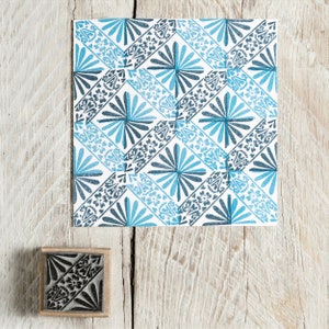May include: A blue and black patterned rubber stamp with a geometric design. The stamp is on a wooden surface.