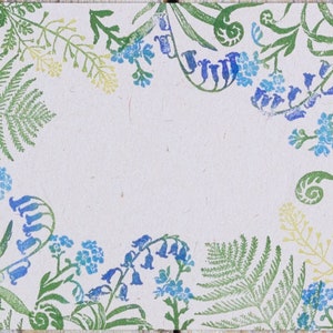 May include: A white background with a green and blue floral border. The border is made up of ferns, leaves, and flowers. The flowers are blue and white.