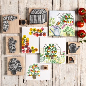 Könnte beinhalten: Eine Sammlung von Holzstempeln mit passenden farbigen Illustrationen, die Gewächshausszenen, Tomatenpflanzen, eine Gießkanne und einen kleinen Vogel zeigen. Vier frische rote Tomaten an einem Zweig befinden sich auf der rechten Seite.