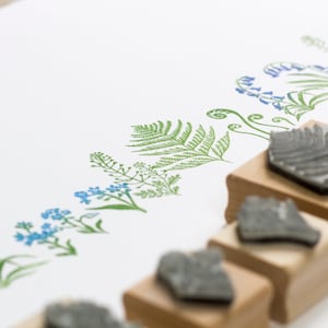 May include: A set of six wooden mounted rubber stamps featuring floral and fern designs. The stamps are arranged in a row on a white surface.