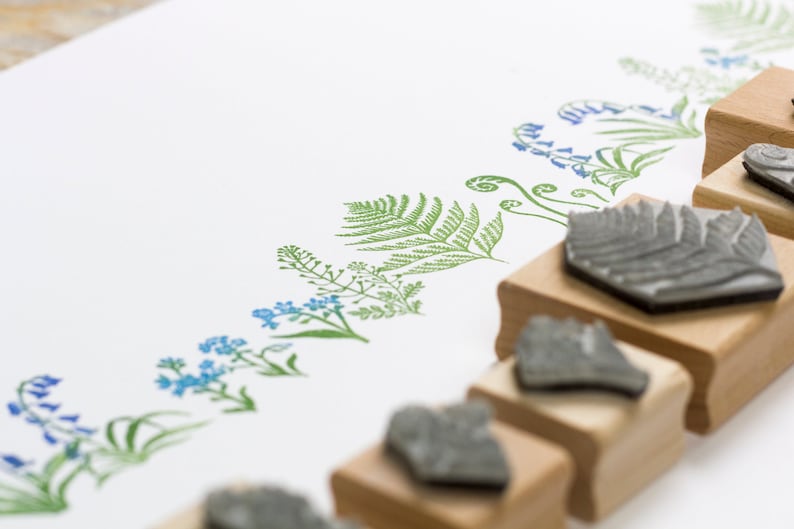 May include: A set of six wooden mounted rubber stamps featuring floral and fern designs. The stamps are arranged in a row on a white surface.