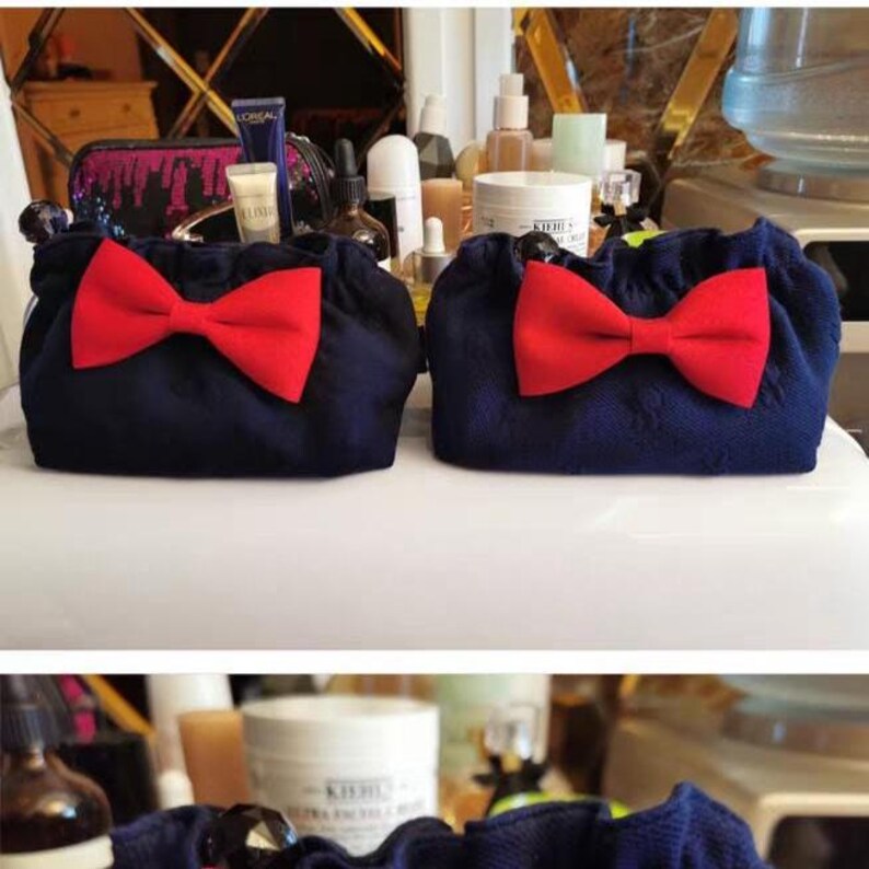 Puede incluir: Dos bolsas de tela azul marino id&eacute;nticas con cierre fruncido en la parte superior y un lazo rojo brillante prominente centrado. Las bolsas tienen una superficie texturizada y est&aacute;n colocadas una al lado de la otra con un dise&ntilde;o uniforme.
