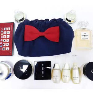 Puede incluir: Una colecci&oacute;n de productos de belleza que incluye un neceser azul marino con un lazo rojo, una paleta Hera rectangular, un frasco de perfume Chanel N&deg;5 cuadrado, un compacto Bobbi Brown, tres frascos Su:m37, un compacto YSL y un compacto Giorgio Armani.