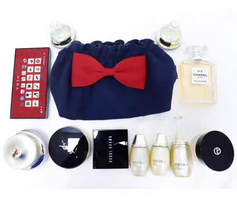 Puede incluir: Una colecci&oacute;n de productos de belleza que incluye un neceser azul marino con un lazo rojo, una paleta Hera rectangular, un frasco de perfume Chanel N&deg;5 cuadrado, un compacto Bobbi Brown, tres frascos Su:m37, un compacto YSL y un compacto Giorgio Armani.