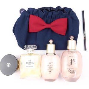 Puede incluir: Una bolsa azul marino con cord&oacute;n y un lazo rojo grande, un recipiente circular negro, un frasco de perfume rectangular Chanel No. 5 Eau Premiere, dos botellas de cuidado facial rosa claro The History of Whoo y un delineador negro Estee Lauder.