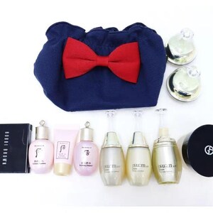 Puede incluir: Un neceser de tela azul marino con un gran lazo rojo, acompa&ntilde;ado de varios productos de cuidado de la piel que incluyen tres frascos Su:m37, dos frascos The History of Whoo, un tubo rosa, un compacto Bobbi Brown, un compacto Giorgio Armani y dos tarros peque&ntilde;os.