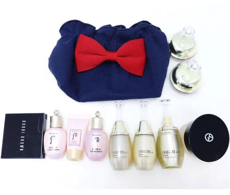 Puede incluir: Un neceser de tela azul marino con un gran lazo rojo, acompa&ntilde;ado de varios productos de cuidado de la piel que incluyen tres frascos Su:m37, dos frascos The History of Whoo, un tubo rosa, un compacto Bobbi Brown, un compacto Giorgio Armani y dos tarros peque&ntilde;os.