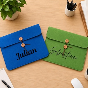 May include: Two rectangular felt document sleeves, one blue and one green, each featuring a flap secured by a brown string wrapped around two wooden buttons. The blue sleeve has the name Julian printed in black, and the green sleeve has Sebastian.