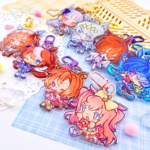 Könnte beinhalten: Eine Sammlung farbenfroher Schlüsselanhänger mit Anime-Charakteren. Jeder Schlüsselanhänger zeigt ein einzigartiges Charakterdesign mit leuchtenden Farben, darunter Pink, Orange, Blau und Lila. Die Schlüsselanhänger haben Metallverschlüsse zur Befestigung.