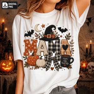 Könnte beinhalten: Ein weißes T-Shirt mit einem Grafikdesign, das das Wort MAMA in verschiedenen Mustern zeigt, dazu ein schwarzer Hexenhut, Kürbisse, eine karierte Schleife, Fledermäuse, eine Mondsichel und eine schwarze Tasse mit der Aufschrift mom life best life.