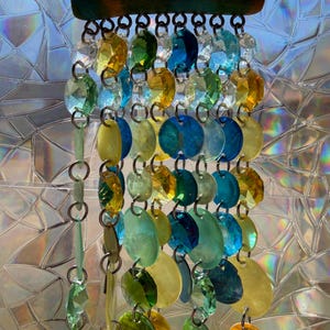 Peut inclure: Un carillon éolien coloré avec un dessus en bois et plusieurs brins de perles de verre iridescentes et d'éléments en forme de coquillage. Les perles et les coquillages sont dans des tons de bleu, jaune, vert et orange, créant une pièce décorative vibrante.