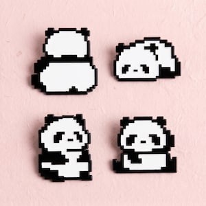 May include: Four enamel pins featuring pixel art designs of pandas in various poses. Each pin is rendered in a high-contrast black and white colour scheme, showcasing distinct blocky, digital-inspired shapes that form the panda figures.