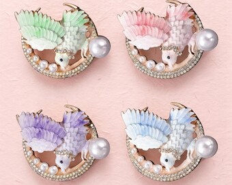 Könnte beinhalten: Vier vogelartige Broschen, jede mit einem halbmondförmigen Rahmen, der mit klaren Strasssteinen und kleinen Perlen besetzt ist. Die Vögel haben strukturierte Flügel in Pastellgrün, Rosa, Violett und Blau sowie eine große Perle an der Seite.