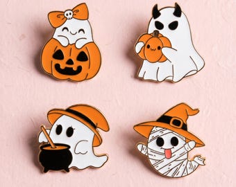 Könnte beinhalten: Vier Emaille-Anstecknadeln mit weißen Geistern im Halloween-Design. Ein Geist trägt eine orangefarbene Schleife, einer hält einen Kürbis, einer rührt in einem schwarzen Kessel mit orangefarbenem Hut und einer ist als Mumie mit Hexenhut dargestellt.