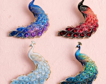 Könnte beinhalten: Vier pfauenförmige Emaille-Broschen mit goldfarbenen Metallrändern. Oben links blau und violett, oben rechts schwarz und rot, unten links weiß und hellblau, unten rechts grün und blau, jeweils mit detaillierten Mustern der Pfauenfedern versehen.