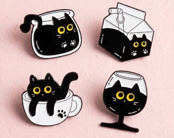 Könnte beinhalten: Vier Emaille-Anstecknadeln mit schwarzen Katzen mit leuchtend gelben Augen. Eine Katze ist in einer Glasschale, eine in einem Milchkarton, eine in einer weißen Teetasse mit Pfotenabdruck und eine in einem Weinglas. Jede Anstecknadel ist schwarz-weiß.