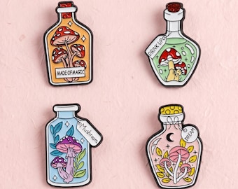 Könnte beinhalten: Vier Emaille-Anstecknadeln in Form von Glasflaschen mit Pilzen. Die Flasche oben links ist orange mit roten Pilzen und dem Text MADE OF MAGIC. Oben rechts ist eine grüne Flasche mit roten Pilzen und dem Text DRINK UP. Unten links ist eine blaue Flasche mit violetten Pilzen und einem Etikett mit der Aufschrift Mushroom. Unten rechts ist eine rosa Flasche mit rosa Pilzen, einem Halbmond und einem Etikett mit der Aufschrift DREAM.