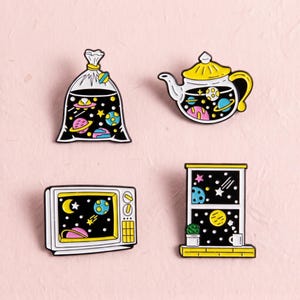 Pode incluir: Quatro pins de esmalte com designs de temática espacial: um saco de plástico, um bule, uma televisão e uma janela. Cada item contém um fundo preto com planetas, estrelas e corpos celestes coloridos em tons de amarelo, rosa e azul.