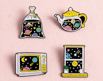 Könnte beinhalten: Vier Emaille-Anstecknadeln mit Weltraum-Motiven: eine Plastiktüte, eine Teekanne, ein Fernseher und ein Fenster. Jeder Gegenstand zeigt einen schwarzen Hintergrund mit bunten Planeten, Sternen und Himmelskörpern in Gelb, Pink und Blau.