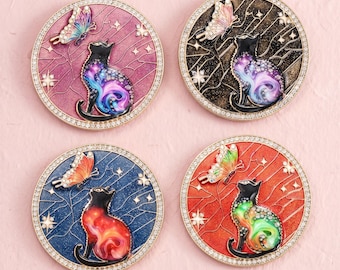 Könnte beinhalten: Vier runde Metallanstecker mit einer Katzensilhouette, einem wirbelnden Galaxiemuster und einem Schmetterling. Die Anstecker haben goldfarbene Ränder mit eingebetteten Kristallen und sind in den Hintergrundfarben Pink, Schwarz, Blau und Orange.