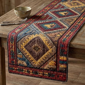 Puede incluir: Camino de mesa acolchado con un patrón geométrico en tonos rojos, dorados, azules y marrones. El camino de mesa presenta formas de diamante y un borde con detalles florales. Un cuenco de madera y cubiertos están sobre la mesa.