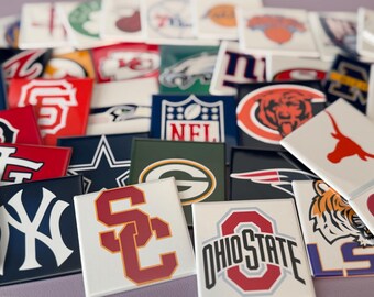 Op de afbeelding: Een verzameling vierkante keramische tegels met logo's van verschillende sportteams, waaronder NFL- en universiteitsteams. De tegels tonen teamkleuren en logo's in diverse ontwerpen, met de nadruk op team branding.