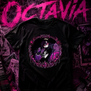 May include: A black t-shirt featuring a circular graphic of a dark-haired character with red eyes, surrounded by a thorny frame with pink accents. The design includes a skull at the bottom and the text OCTAVIA in large pink letters at the top.