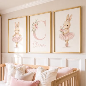 May include: Three framed wall art prints featuring watercolor illustrations of a rabbit in a pink tutu. The center print displays a large pink letter C with floral accents and the name Clara written in a cursive script below the letter.