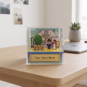 May include: A pixel art diorama in a clear acrylic box. The scene depicts a wedding with a house, tree, and sunflowers. The text "Your Farm Name" is on a banner at the bottom. The figures are a bride and groom.