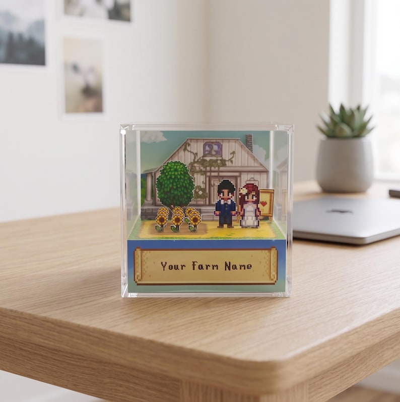 May include: A pixel art diorama in a clear acrylic box. The scene depicts a wedding with a house, tree, and sunflowers. The text "Your Farm Name" is on a banner at the bottom. The figures are a bride and groom.