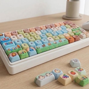 May include: A white mechanical keyboard with colorful keycaps. The keycaps feature pastel colors and illustrations of animals and scenes. Additional keycaps with animal and fruit designs are scattered around the keyboard.
