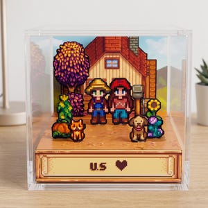 Könnte beinhalten: Ein pixeliges Diorama mit einer Farm-Szene mit einem Haus, zwei Figuren, einer Katze und einem Hund. Auf der Basis der Anzeige steht "U.S. ❤". Die Szene ist in einer transparenten Acrylbox eingeschlossen, die auf einer Holzoberfläche steht.