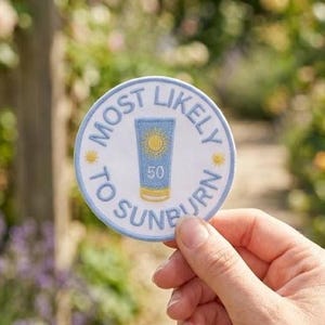 May include: A circular embroidered patch with a white background and a light blue border. The center features a blue sunscreen bottle graphic with a yellow sun icon and the number 50. The text MOST LIKELY TO SUNBURN circles the graphic.